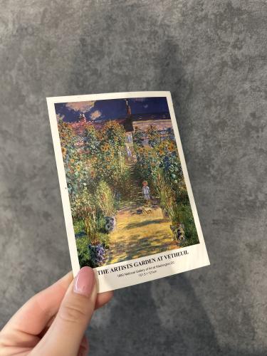 Hand holding a postcard with a picture of a rural landscape.