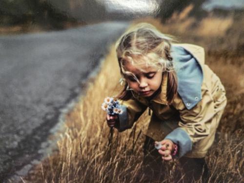Little girl with flowers on the road. Photo in old color image style.