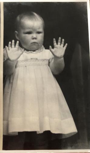 A vintage photo of a little girl wearing a white dress and a black background