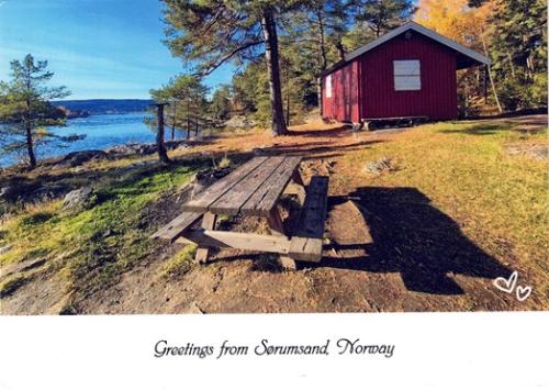 Wooden bench on the shore of a lake in Norway with a red cabin in the background