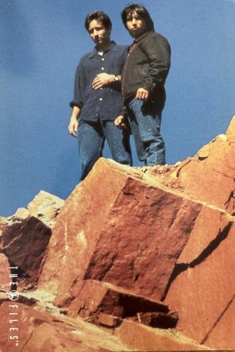 Father and son standing on the top of a rock.  They are wearing jeans and a black shirt.