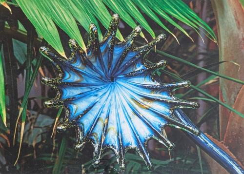 Blue metal flower on the background of palm leaves in the garden.